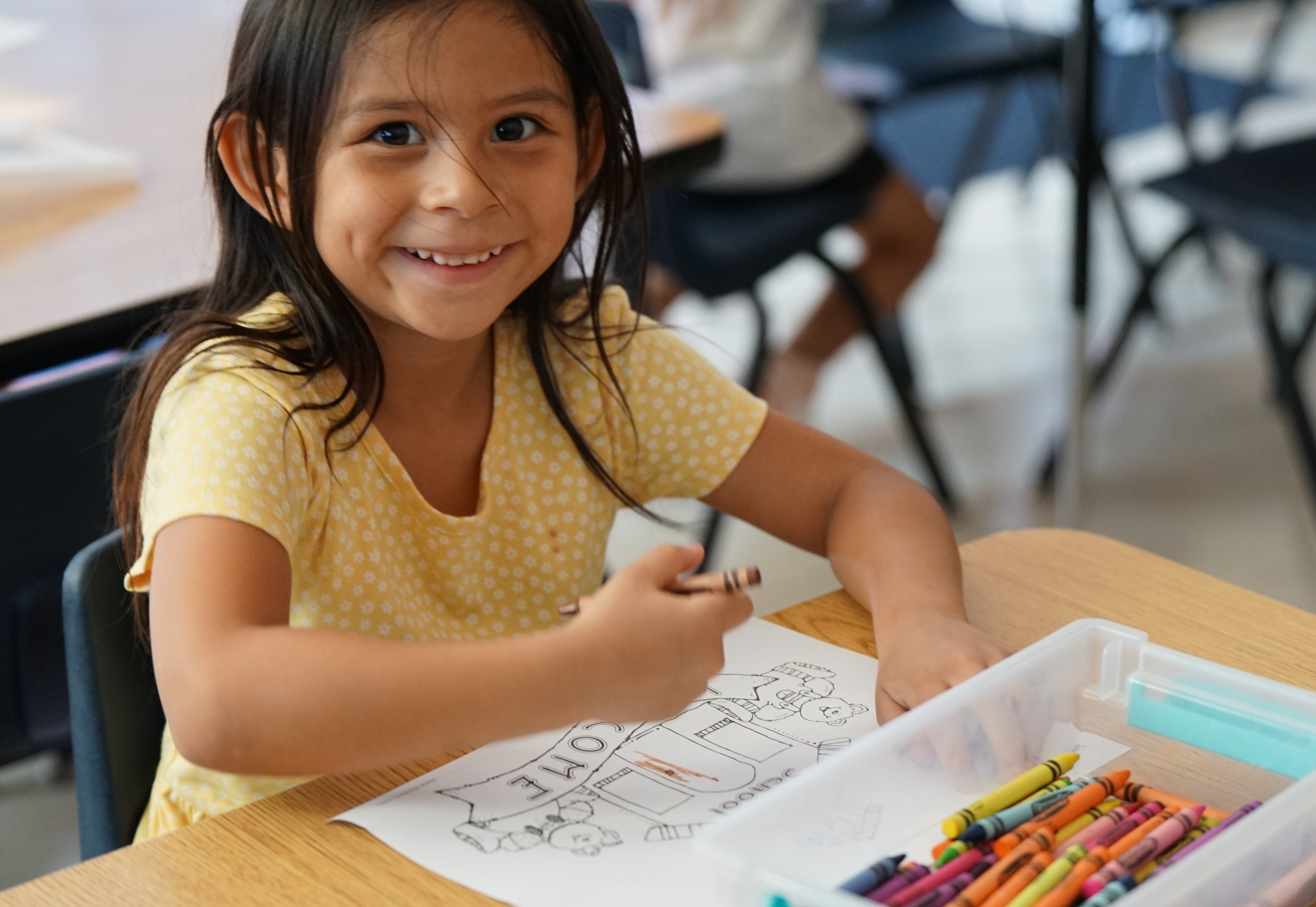 A little girl smiles as she holds a crayon, getting ready to color her paper