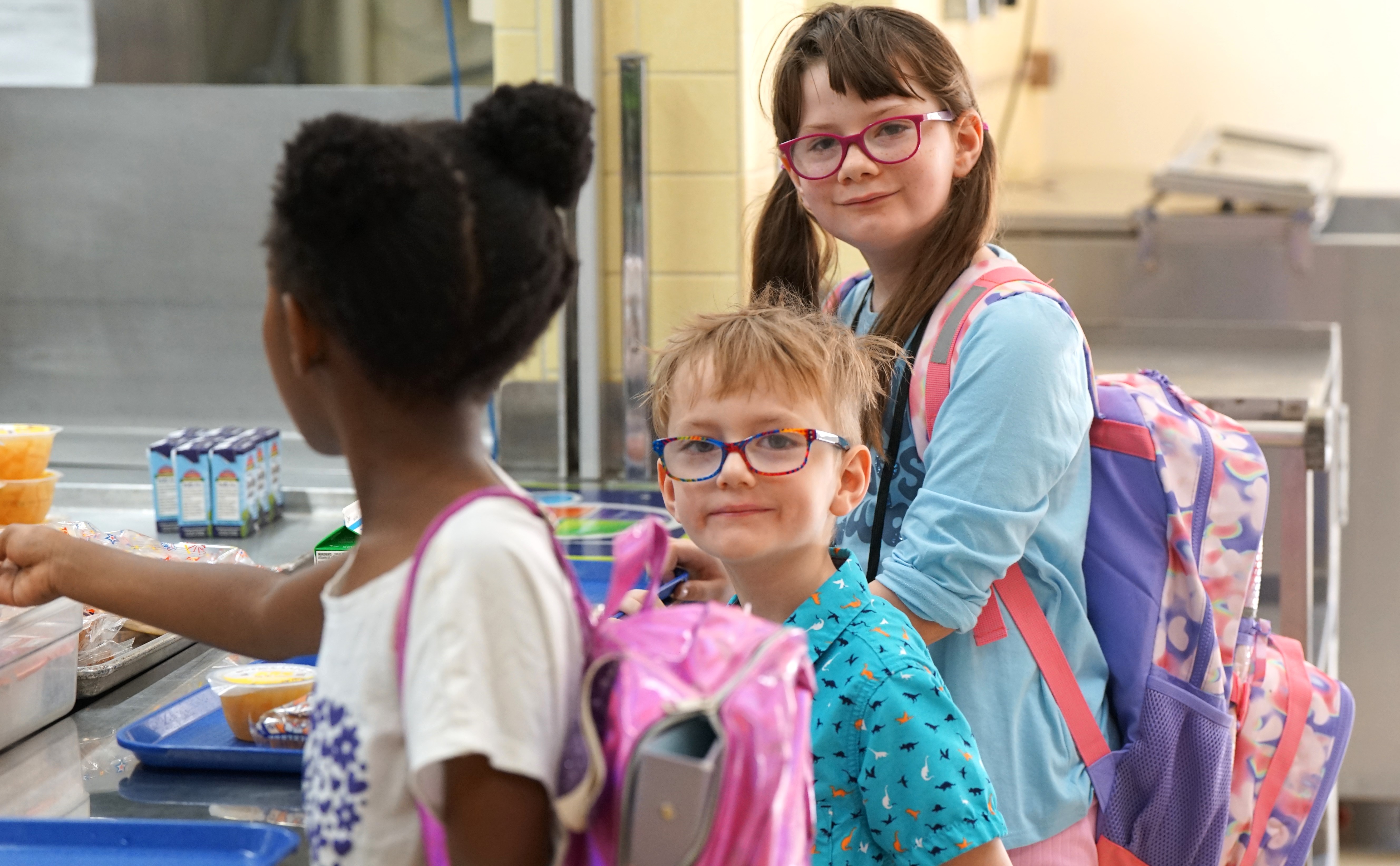 Three kids stand in line to get their lunch in the cafeteria