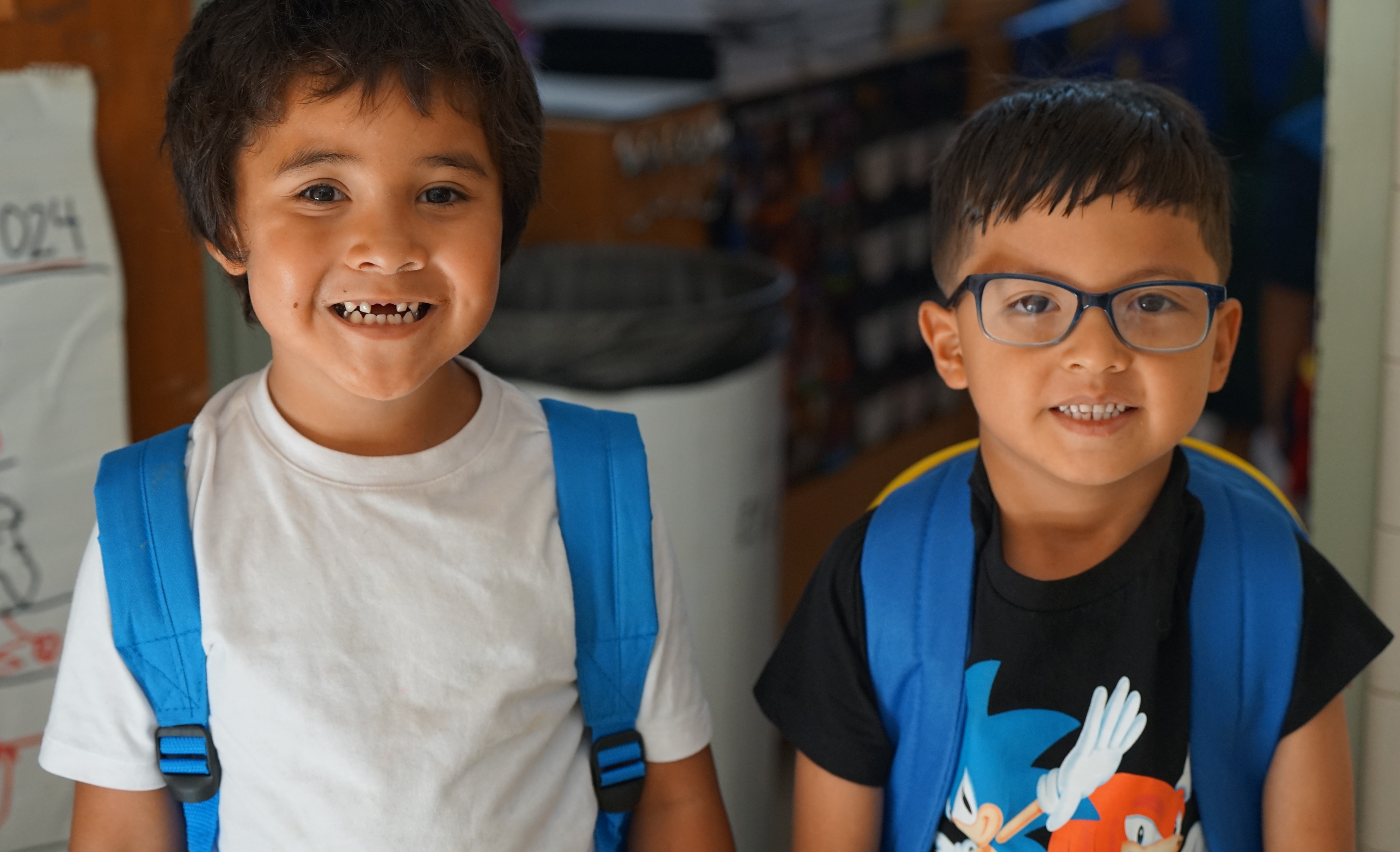 Two boys smile with their blue backpacks on