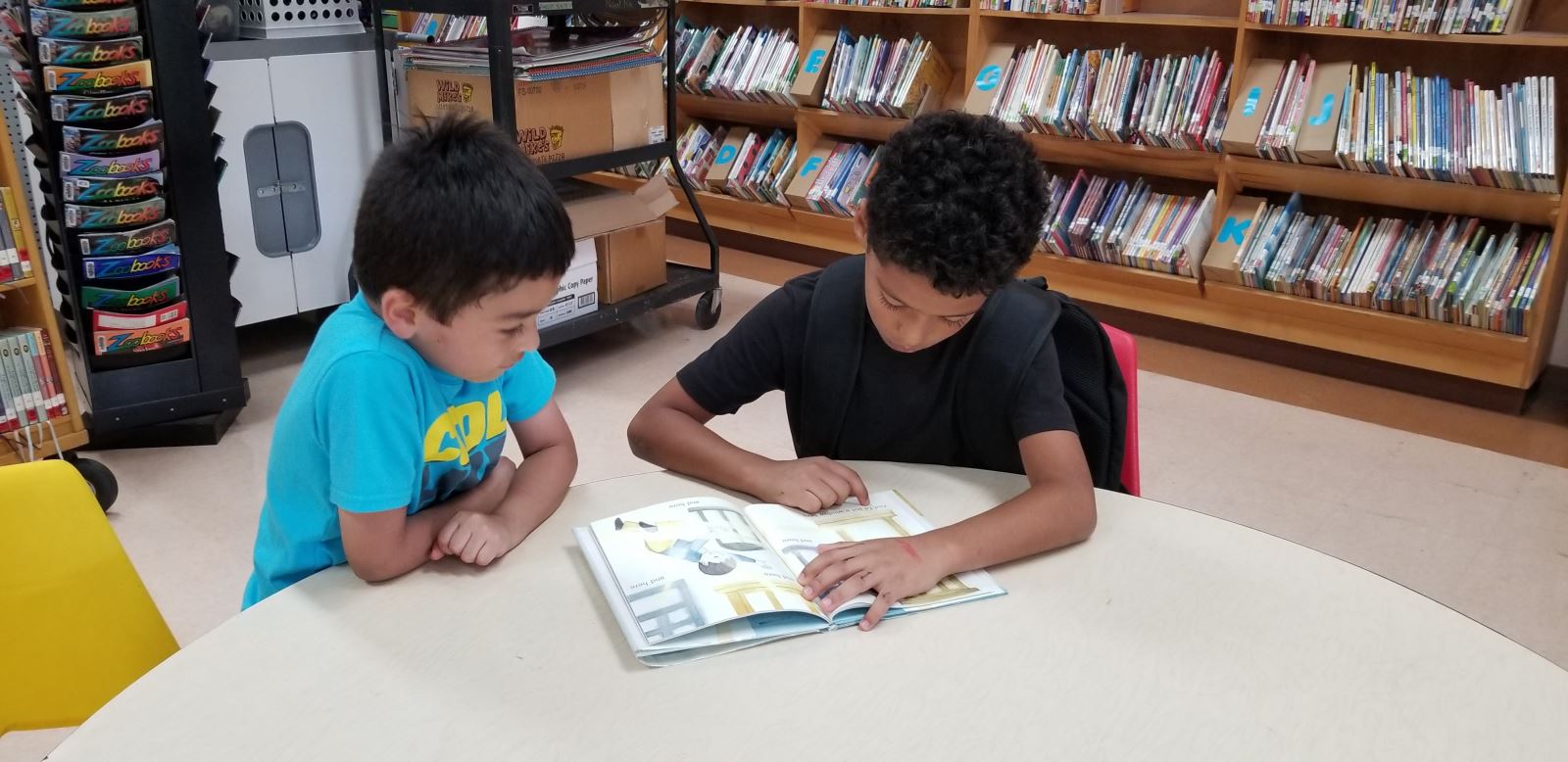 Two students read together at a table in the library